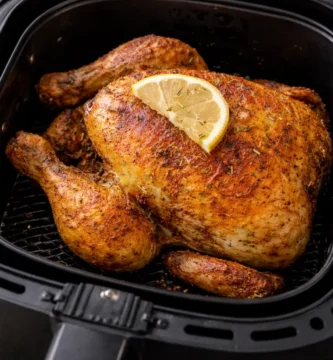 Pollo entero dorado y crujiente cocinado en freidora de aire con limón y especias dentro de la cesta