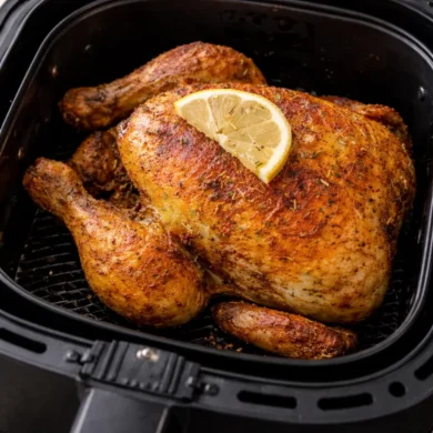 Pollo entero dorado y crujiente cocinado en freidora de aire con limón y especias dentro de la cesta